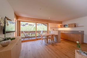 Een moderne keuken met houten kastjes, een eethoek met tafel en stoelen, en een grote schuifdeur die uitkomt op een terras.