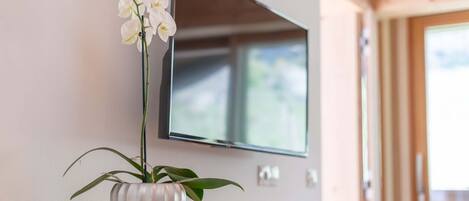Un televisor de pantalla plana montado en una pared, una orquídea en maceta sobre una consola de madera, y una puerta que da al exterior.