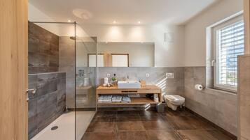 A modern bathroom with a glass shower enclosure, a wooden vanity, a toilet, and a large window.