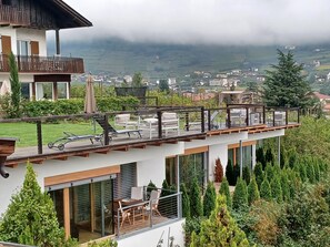 Un edificio moderno de dos pisos con balcón, asientos al aire libre y vistas a un valle.