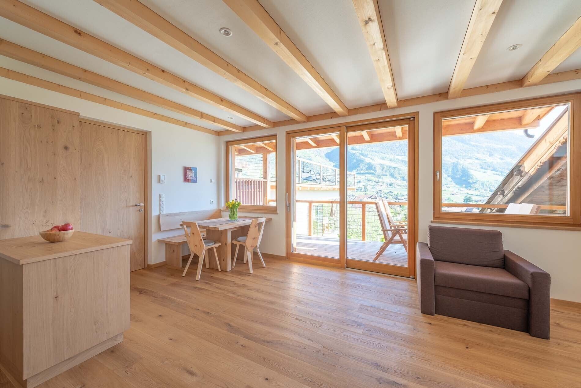 Ein geräumiges Zimmer mit Holzböden, einer Essecke mit Tisch und Stühlen, einem Sofa und großen Fenstern mit Blick auf die Berge.
