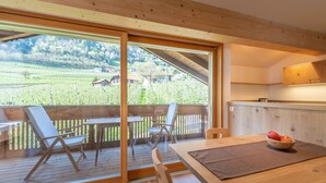 A wooden deck with a table and chairs, a bowl of fruit, and a view of a vineyard. - Chalet 'Moosbichlerhof  Rosalia' with Mountain View, Shared Pool and Wi-Fi (Marling)
