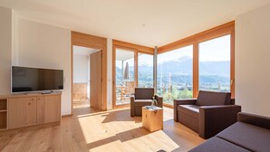 A modern living room with a flat-screen TV, wooden furniture, and large windows offering a mountain view. - Chalet 'Moosbichlerhof  Rosalia' with Mountain View, Shared Pool and Wi-Fi (Marling)