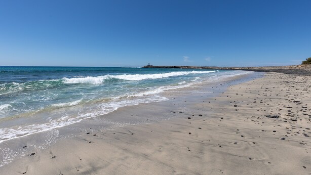 A beach with a lighthouse in the distance, sandy shore, and waves. - Vacation Home 'Buganvilla' with Sea View and Wi-Fi (Pájara)
