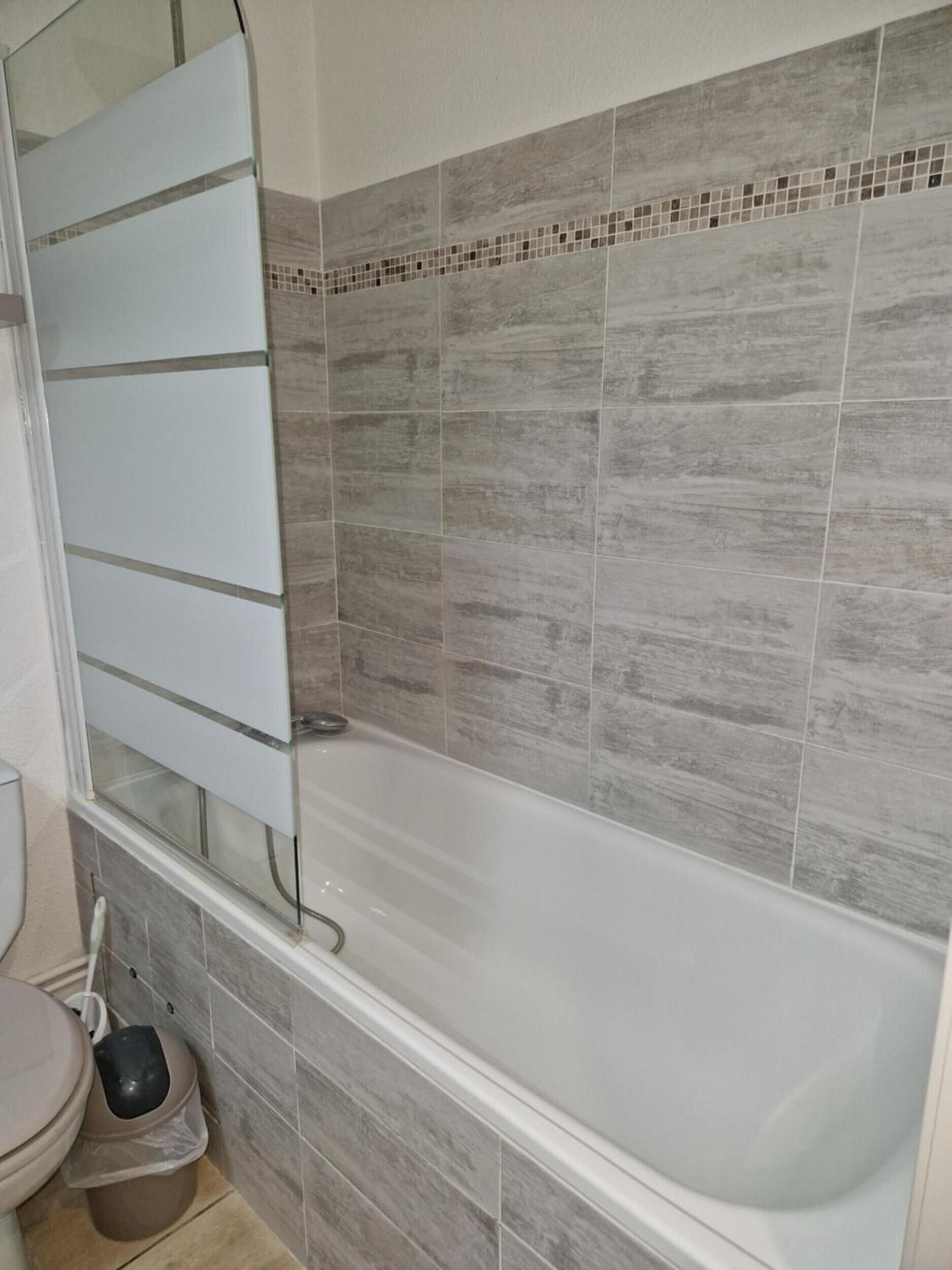 A bathroom with a bathtub, toilet, and a trash bin.