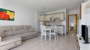 A modern living room with a sofa, dining table, and chairs, a kitchen with cabinets and a microwave, and a TV on a stand. - Escapada Al Sur Vacation Apartment with Wi-Fi (Morro del Jable)