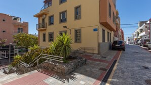 A multi-story building with a flat facade, a visible balcony, and a paved street with cars parked along the side. - Escapada Al Sur Vacation Apartment with Wi-Fi (Morro del Jable)