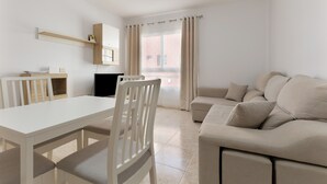 Ein modernes Wohnzimmer mit einem weißen Sofa, einem Esstisch mit Stühlen, einem Fernseher und einem Fenster mit Vorhängen.