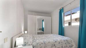 Ein Schlafzimmer mit Bett, Nachttisch, Lampe und einem Fenster mit Vorhängen.