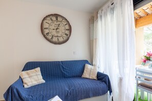 A room with a blue-striped sofa, a wall clock, and a window with curtains. - Studio 'Sanary Soleil Et Douceur 3' with Shared Pool, Wi-Fi and Air Conditioning (Sanary-sur-Mer)