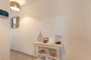 A hallway with a white wall, a small table with a mirror, a hanging light fixture, and a sign indicating a touristic area. - Studio 'Sanary Soleil Et Douceur 3' with Shared Pool, Wi-Fi and Air Conditioning (Sanary-sur-Mer)