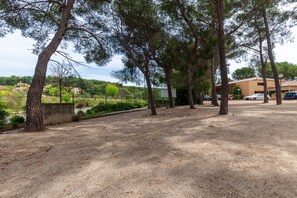 A gravel path lined with tall trees, a building with a flat roof, and parked cars. - Studio 'Sanary Soleil Et Douceur 3' with Shared Pool, Wi-Fi and Air Conditioning (Sanary-sur-Mer)
