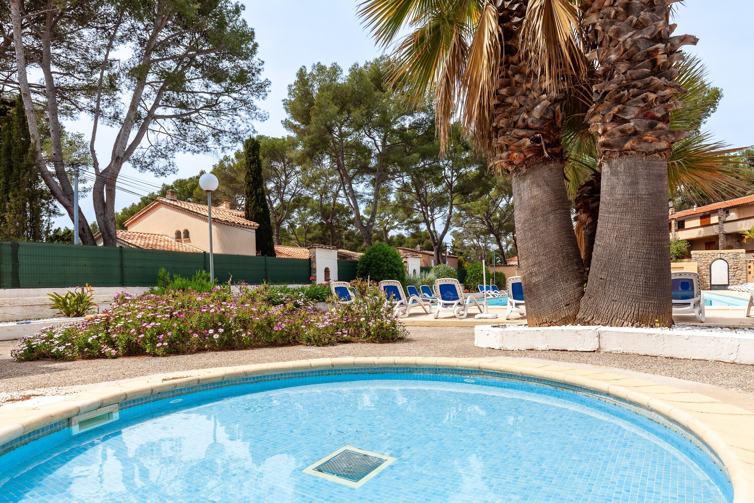 Ein Swimmingpool mit Liegestühlen, Palmen und einem Gebäude im Hintergrund.