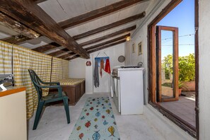A compact kitchen with a wooden ceiling, a washing machine, a refrigerator, and a window leading to an outdoor area.