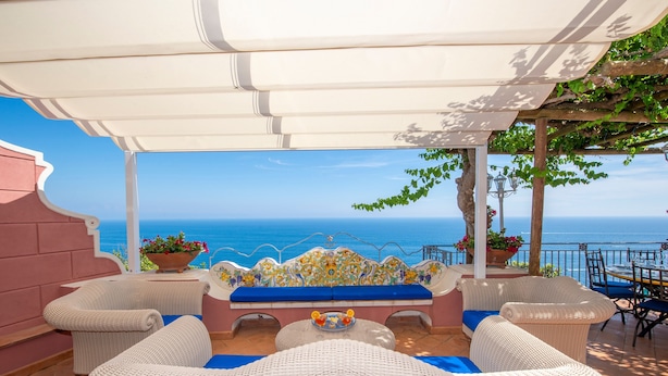 A covered outdoor seating area with wicker furniture, a table with fruit, and a view of the sea. - Villa 'Luxury  Soleluna Con Jacuzzi' with Sea View, Wi-Fi and Air Conditioning (Praiano)