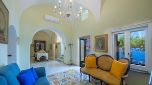 A living room with a blue sofa, a yellow armchair, a patterned rug, and a chandelier. - Villa 'Luxury  Soleluna Con Jacuzzi' with Sea View, Wi-Fi and Air Conditioning (Praiano)