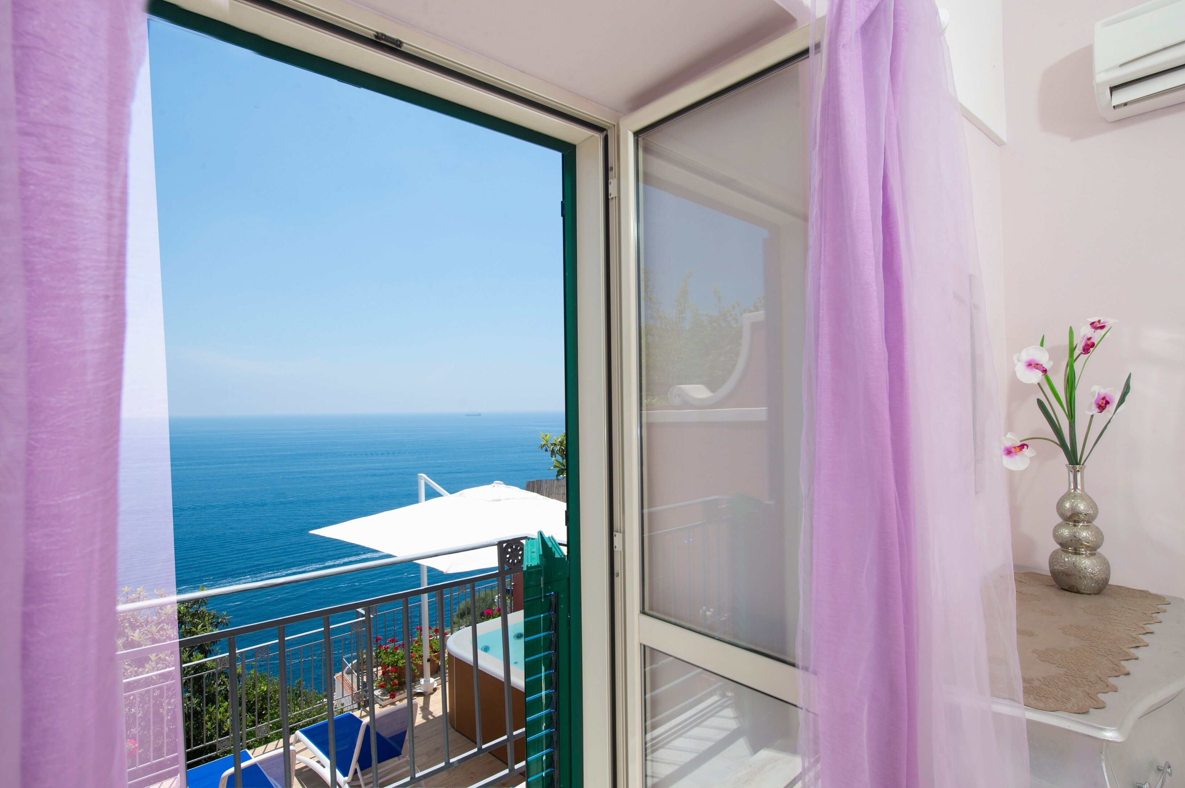 Un balcón con vistas al mar, un equipo de aire acondicionado blanco y un florero con flores.