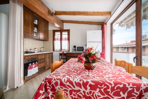 Une cuisine avec des meubles de rangement en bois, une table à manger recouverte d’une nappe rouge et blanche, et un vase à fleurs.
