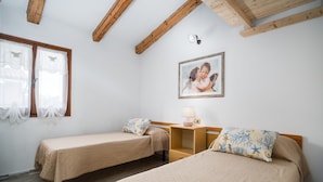 Een kamer met twee eenpersoonsbedden, een houten nachtkastje, een wandlamp en een lijst met een afbeelding.