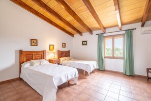 Une chambre avec deux lits, des poutres en bois au plafond, une fenêtre avec des rideaux et un climatiseur fixé au mur.