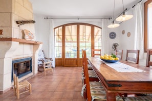 Un comedor con mesa de madera, sillas, chimenea y vistas a través de un ventanal.