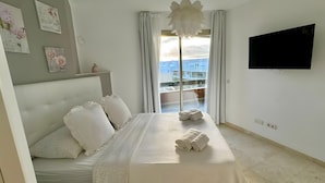 A bedroom with a bed, a TV, a balcony with curtains, and a city view. - Vacation 'Dream Home Beny' with Sea View, Wi-Fi and Air Conditioning (Palm-mar)
