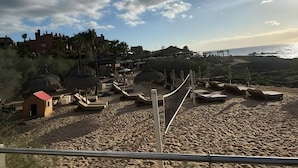 A beach with a volleyball net, lounge chairs, and thatched umbrellas. - Vacation 'Dream Home Beny' with Sea View, Wi-Fi and Air Conditioning (Palm-mar)