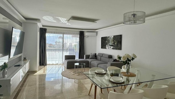 A modern living room with a glass dining table, grey sofas, a TV, and a large window with curtains. - Vacation 'Dream Home Beny' with Sea View, Wi-Fi and Air Conditioning (Palm-mar)