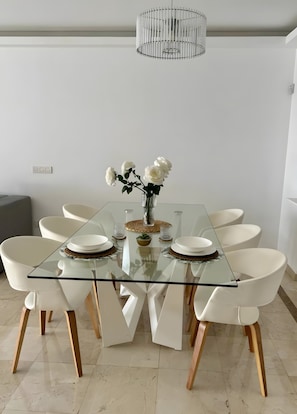 Un espace repas moderne avec une table en verre, des chaises blanches et un luminaire suspendu.