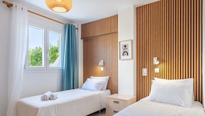 Une chambre d’hôtel avec deux lits, une fenêtre avec des rideaux, une table de chevet avec une lampe et un mur avec des lambris en bois verticaux.