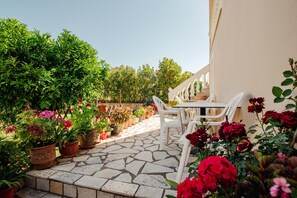 A patio with stone flooring, white chairs, and potted plants.