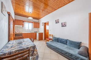 Uma sala de estar aconchegante com sofá e mesa de jantar, teto de madeira e cozinha ao fundo.