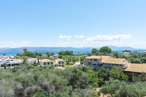 Uma área residencial costeira com casas, algumas com varandas, e uma vista clara do mar e montanhas ao fundo.