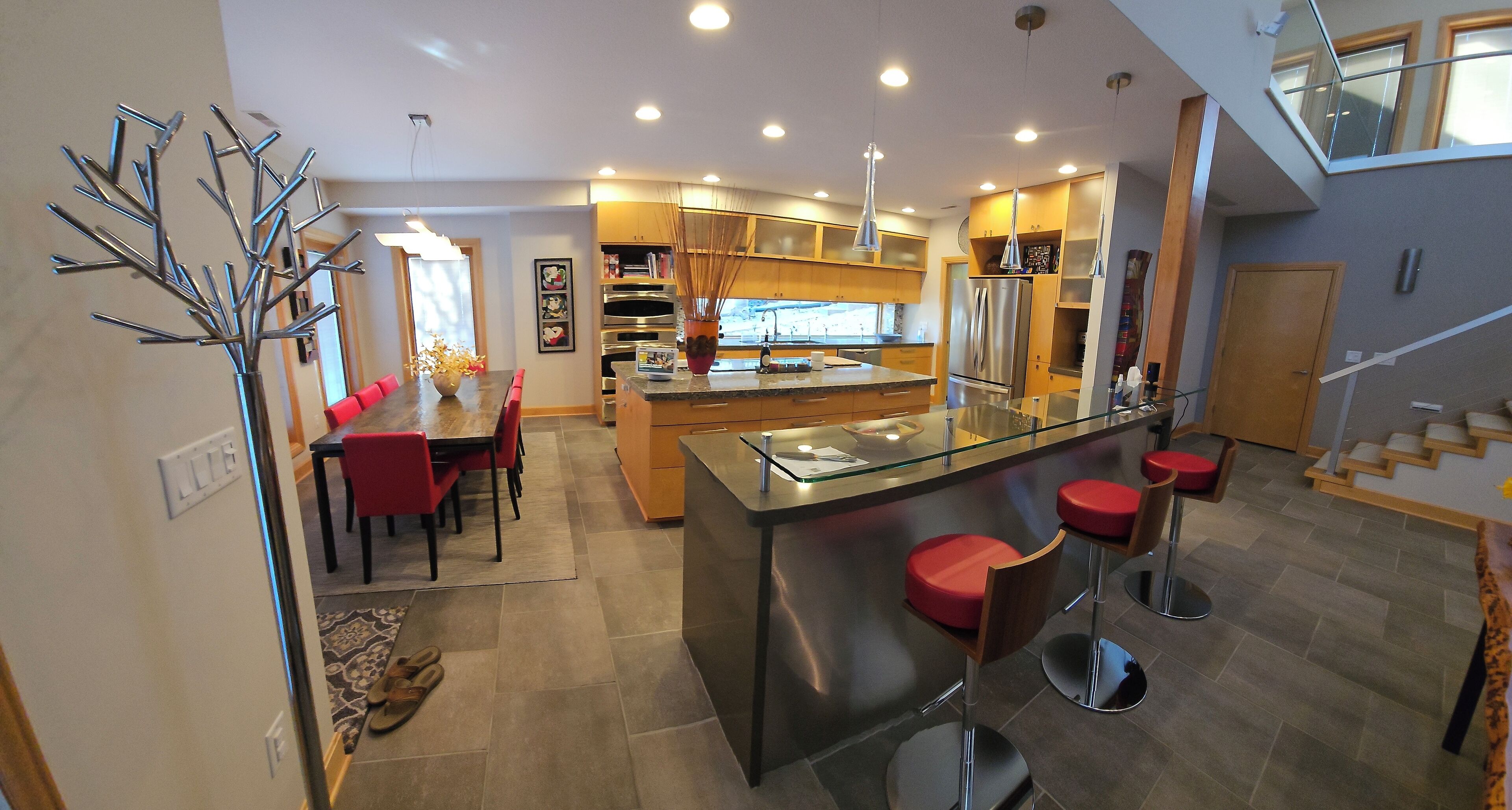 A modern kitchen with a central island, bar stools, and a dining area with red chairs.