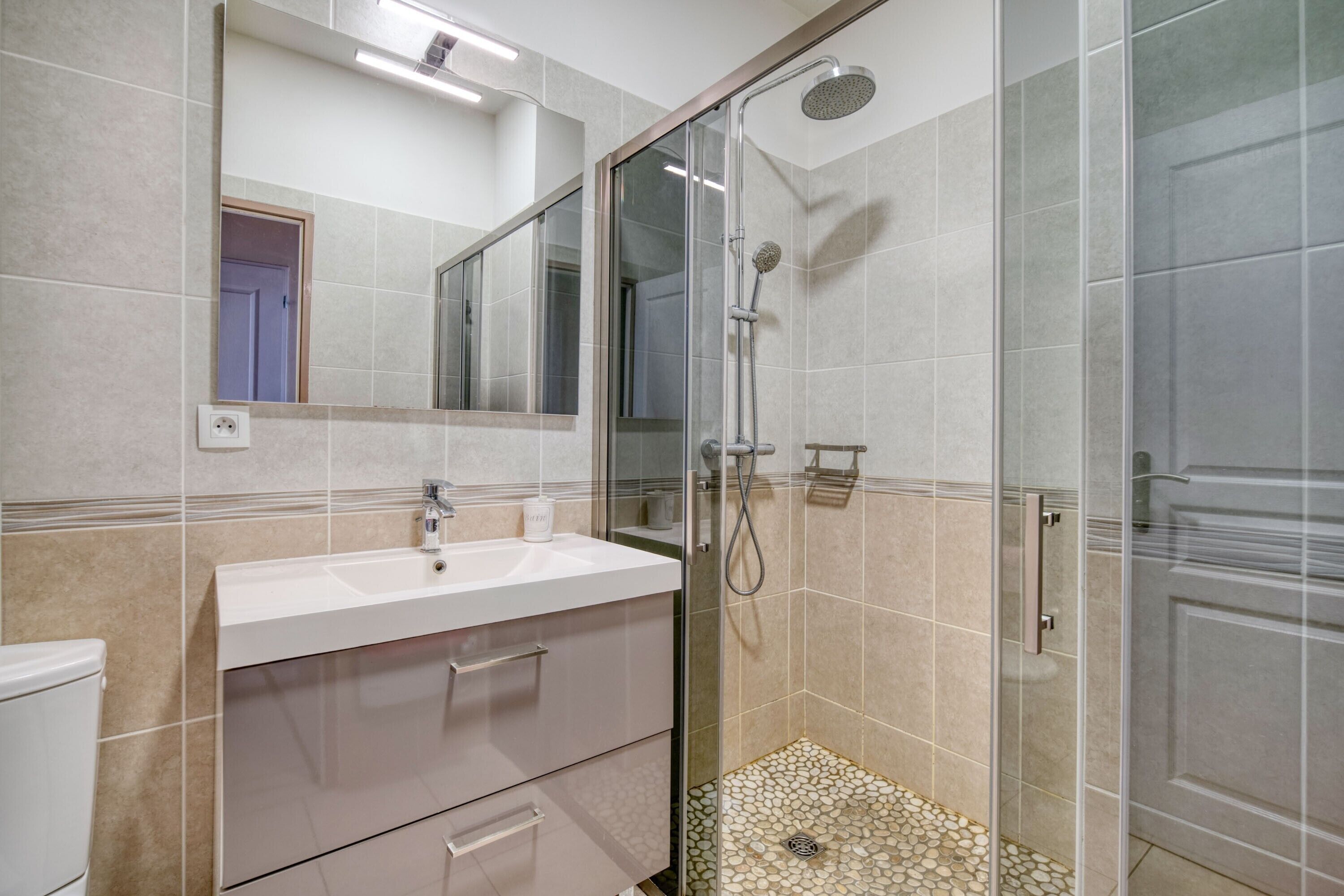 Une salle de bain avec une douche à parois de verre, un lavabo blanc et un miroir au-dessus.