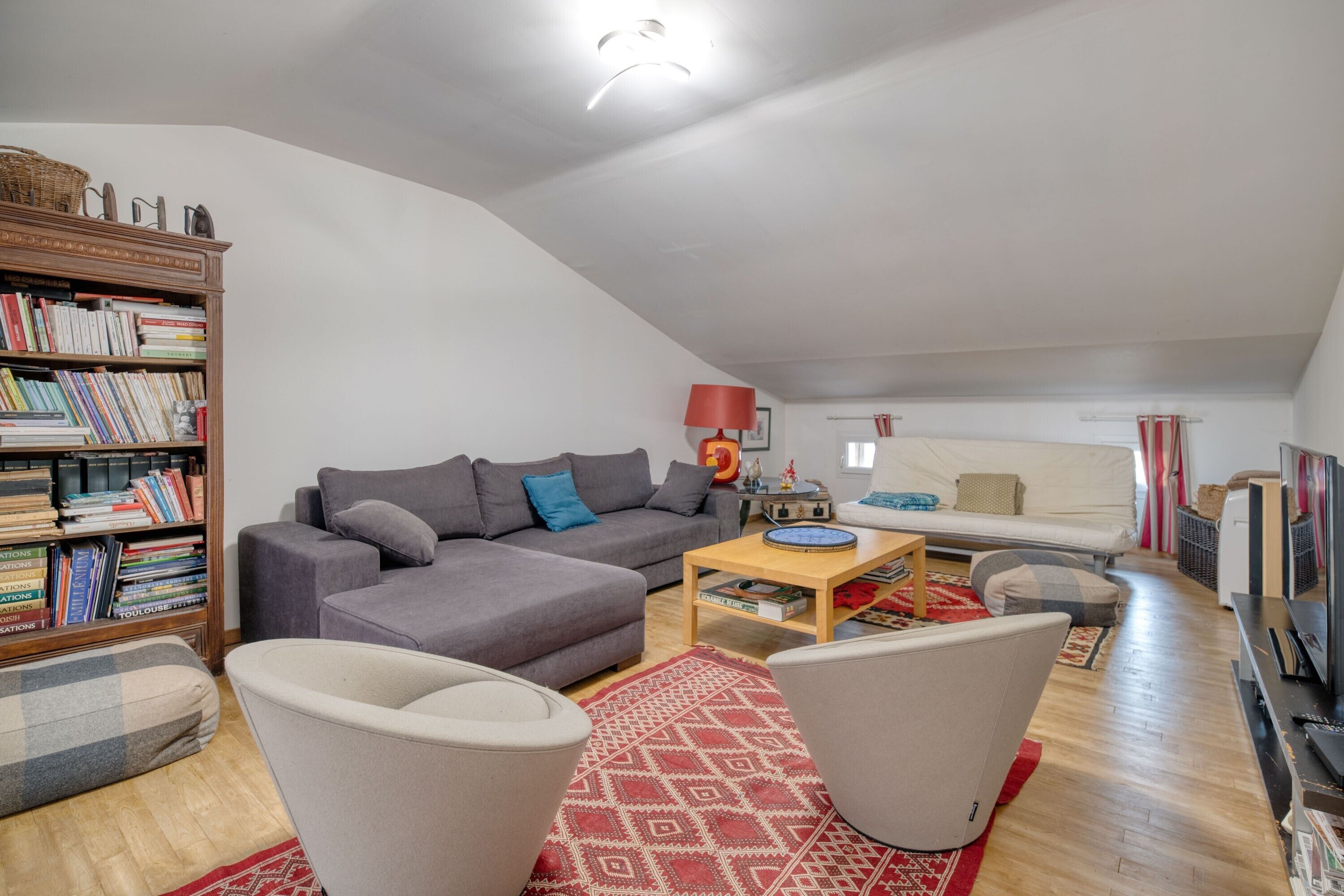 Un salon comprenant un canapé, des fauteuils, une table basse, une bibliothèque et un téléviseur.