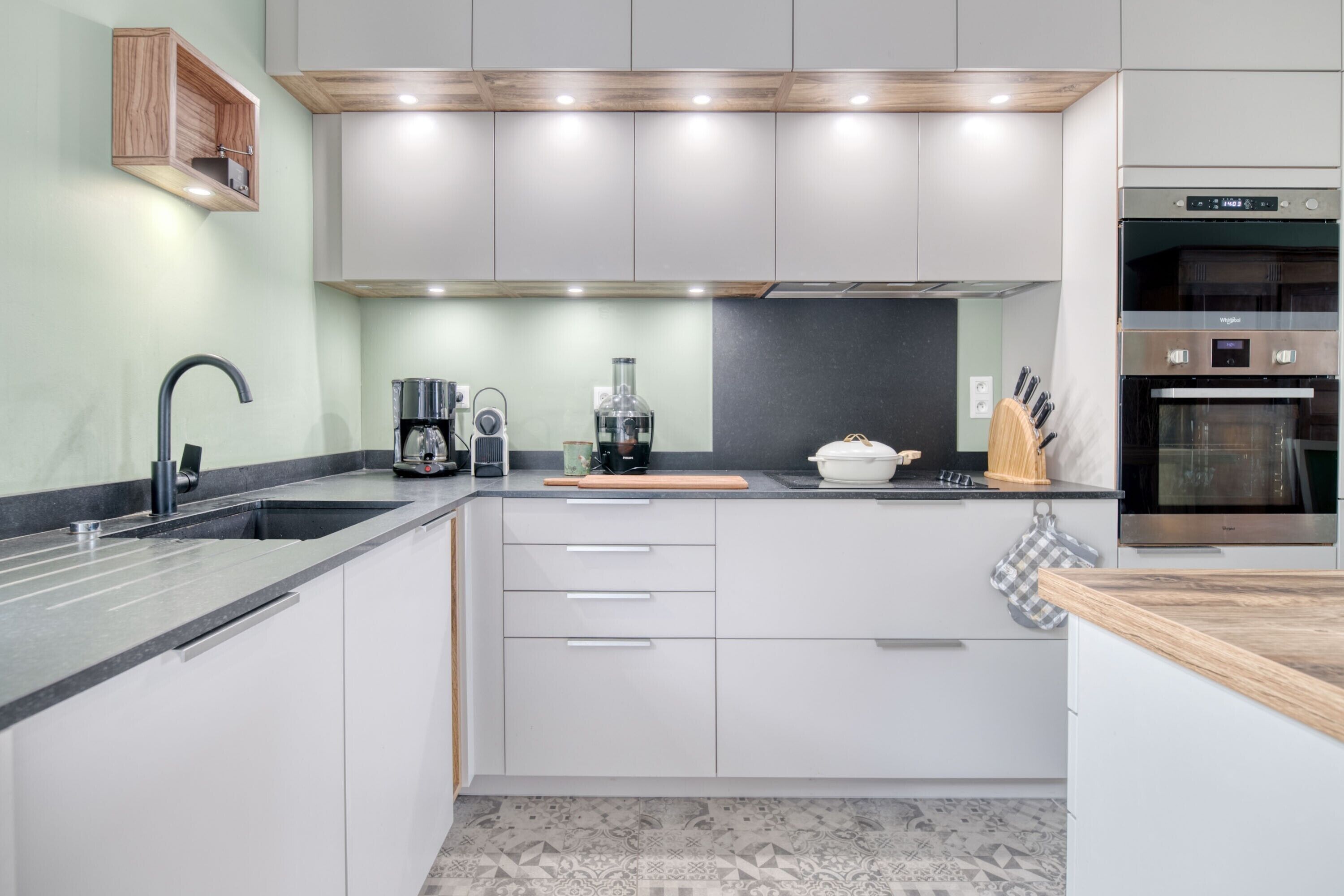 A modern kitchen with white cabinets, a stainless steel oven, and a coffee maker.