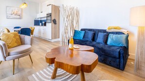 A modern living room with a sofa, armchair, coffee table, and a kitchen area in the background.