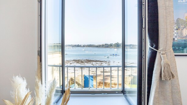 A room with a large window overlooking a beach and the sea.