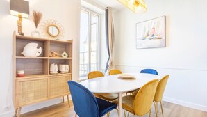 A dining area with a round table, blue and yellow chairs, a wooden console table with decorative items, and a large window with curtains.