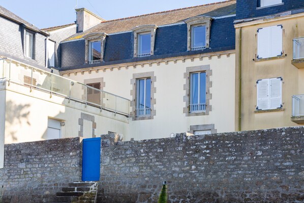 A multi-story building with a stone wall, a blue door, and a staircase leading to an upper level.