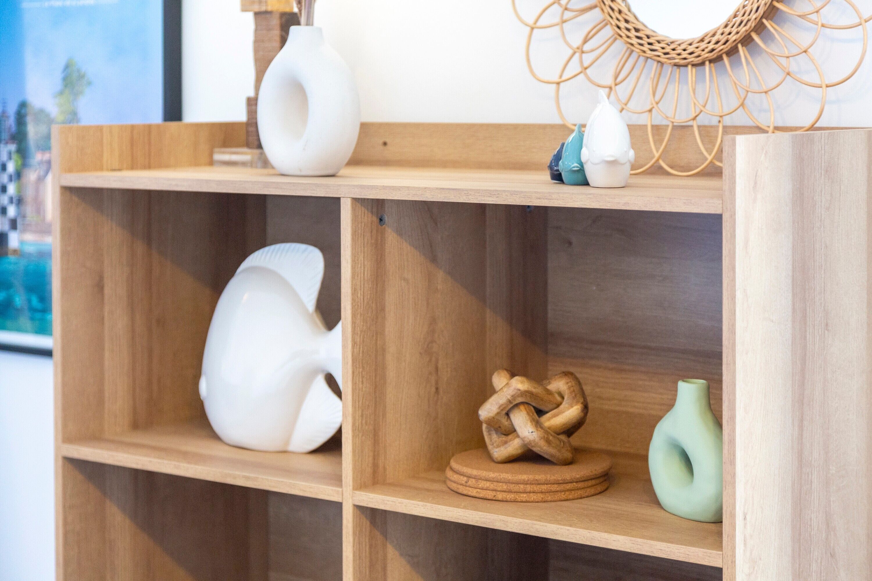 Un estante de madera con diversos objetos decorativos, incluyendo un jarrón blanco, una escultura de madera y un jarrón verde.