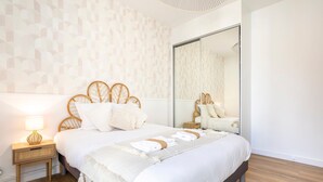 A neatly arranged bedroom with a bed, bedside table, lamp, and a large mirror.