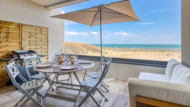 Un comedor con mesa, sillas y una parrilla, con vista a la playa.