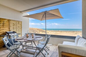 A dining area with a table, chairs, and a grill, overlooking a beach.