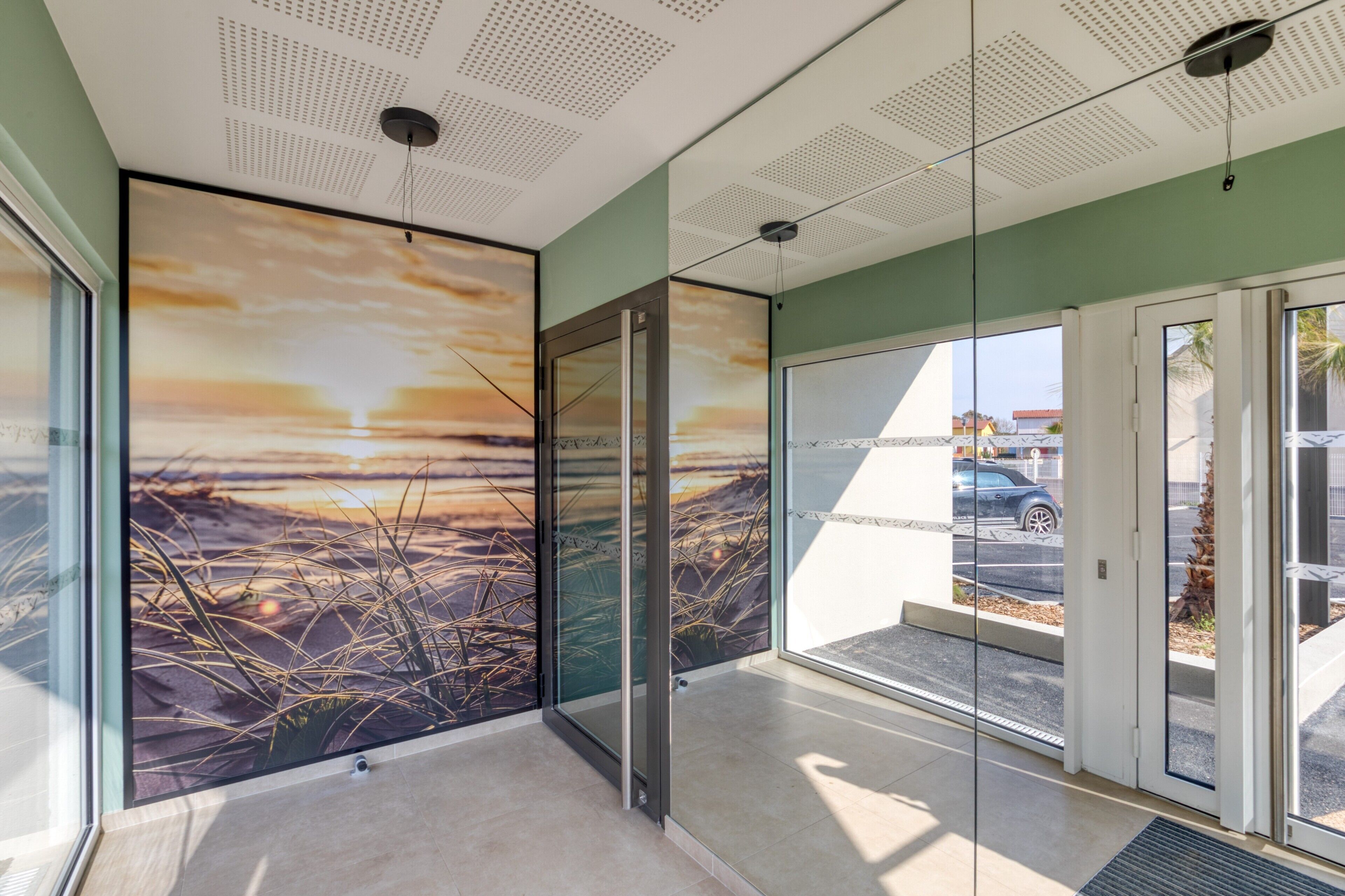 Ein modernes Interieur mit Glastür zum Außenbereich, einer Decke mit Rasterstruktur und einem großen Wandbild, das einen Sonnenuntergang zeigt.