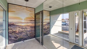 Un interior moderno con un vidrio que da a un espacio exterior, un techo con diseño de cuadrícula y un mural grande que representa un atardecer.