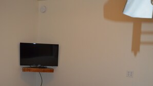Een slaapkamer met een bed, een aan de muur bevestigde televisie en een stopcontact.