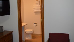 Een hotelkamer met een houten deur naar een badkamer, een houten stoel en een televisie op een dressoir.