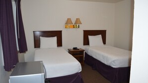 Een hotelkamer met twee enkele bedden, een tafeltje, een lamp en een koelkast.